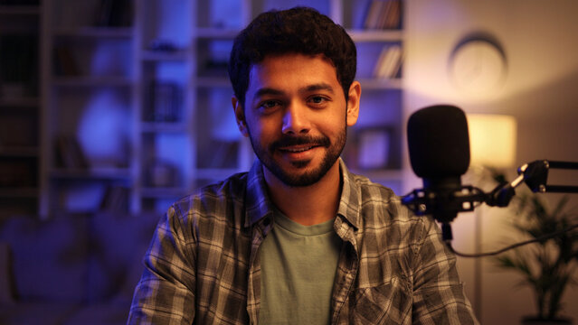 Portrait of young confident Arab man playing online computer video game, live streaming at home, smiling and looking at camera. Gamer lifestyle, E-Sport online gaming technology concept.