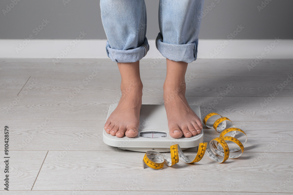 Poster Eating disorder. Woman standing on floor scale and measuring tape indoors, closeup