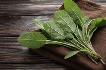 Napkin with green sage leaves on wooden table, closeup