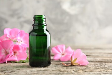 Bottle of geranium essential oil and beautiful flowers on wooden table, closeup. Space for text