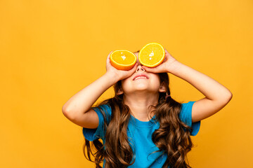Close up studio portrait of child smiling, holding halves of citrus fruit oranges at her eyes on yellow background. Holiday, summer, fashion concept. Copy space