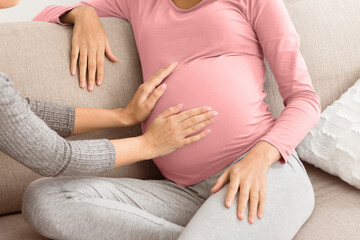 Woman visit pregnant friend and touching belly feeling baby moving, closeup