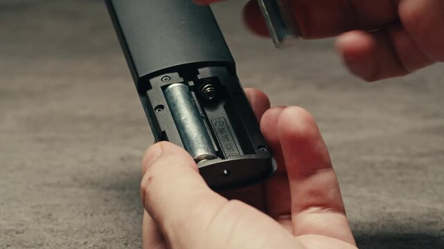Adding silver batteries AA and AAA in remote controller TV close-up. Batteries are common in portable electronic devices. An AA battery is composed of a single electrochemical cell that may be either