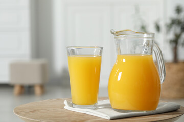 Tasty orange juice in jug and glass on wooden table. Space for text