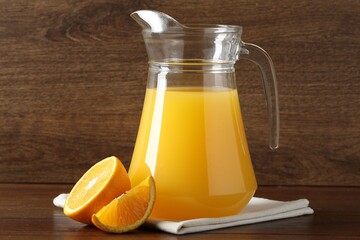 Tasty orange juice in jug and citrus fruit on wooden table, closeup