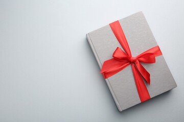 Book tied with red ribbon on grey background, top view with space for text. Perfect gift