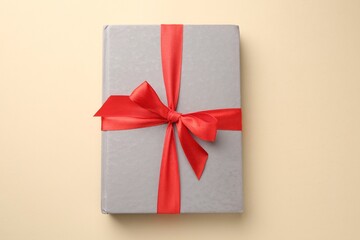 Book tied with red ribbon on beige background, top view. Perfect gift