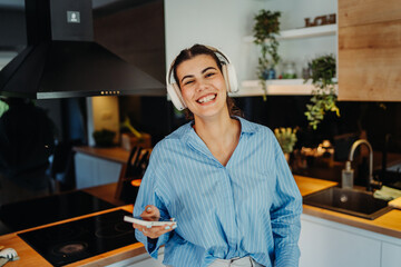 Young caucasian woman singing with whisk listening to music in kitchen
