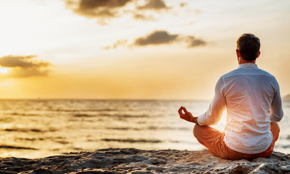 man sitting, meditating in yoga position near ocean beach in beautiful sunrise peaceful time