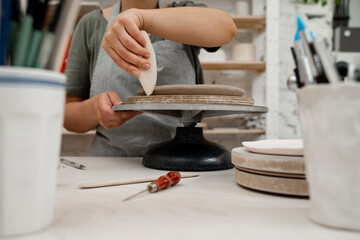 Crafting smooth angle conversion and textured ribs with a clay pottery scrapper. Girl is using a pottery scrapper to smooth the edges of a clay product.