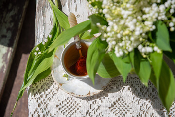 cozy still life with breakfast, hot tea in an antique porcelain cup and a bouquet of lilies of the valley in an antique vase,