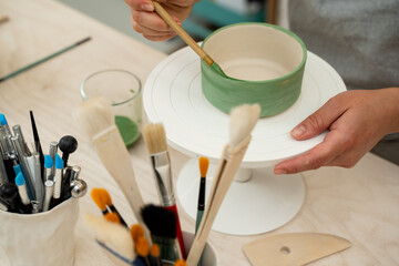 Using a brush to paint a ceramics bowl. Learning how to paint a handmade pottery project. Girl is decorating a clay product with bright green color.