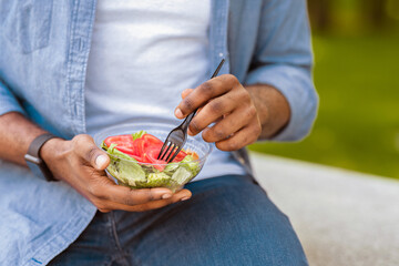 Healthy Dieting. Unrecognizable Black Man Eating Fresh Vegetable Salad Outdoors, Having Business Lunch In Park, Cropped Image, Closeup