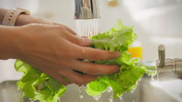 Food. Young man in home clothes concentratedly cleans fresh lettuce in home kitchen. Female athlete washes lettuce under water current approaches to cooking healthy food, splashes