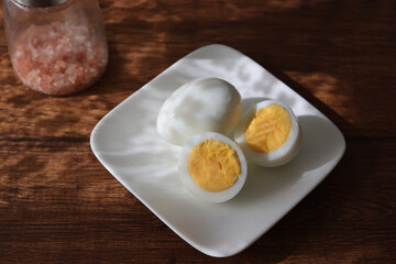 皿にのせ木製テーブルにおいたゆで卵と岩塩