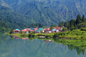 カラフルな屋根が並ぶ大志集落を抜ける只見線気動車と只見川のリフレクション