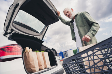 Photo of handsome good mood seniour guy wear green shirt putting bargains inside car outdoors urban city street