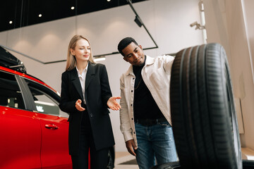 Low-angle view of saleswoman in business suit talking about characteristic of tires product to...