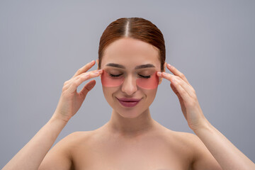 Fototapeta premium Cute young woman using beauty patches under her eyes and looking contented