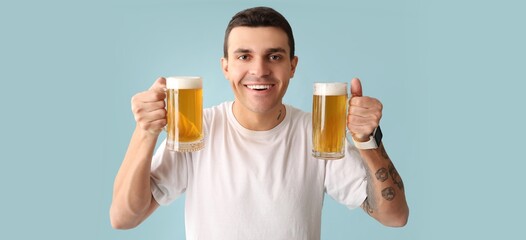 Handsome young man drinking beer on light blue background