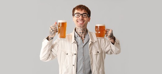 Young tattooed man drinking beer on light background