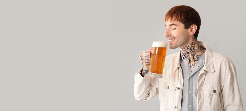 Young tattooed man drinking beer on light background with space for text