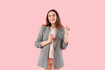 Pretty young woman with smartphone pointing at something on pink background
