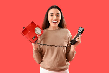 Pretty young woman with telephone on red background