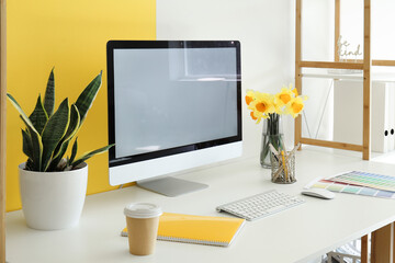 Modern PC, beautiful narcissus flowers, houseplant, coffee, notebook and paint color palettes on...