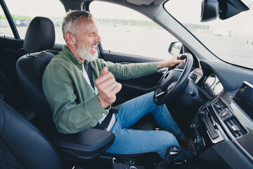 Photo of attractive funny retired guy wear khaki shirt driving automobile having fun outdoors urban...