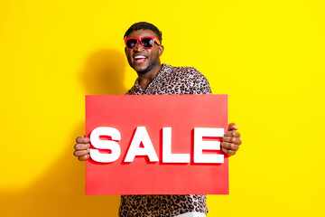 Photo of cool cheerful man wear trendy clothes showing placard summer sale isolated on yellow color...