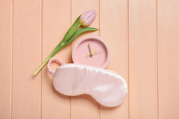 Sleep mask, tulip flower and alarm clock on pink wooden background