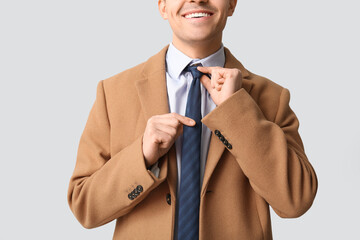 Smiling young man straightening his tie on white background. Closeup