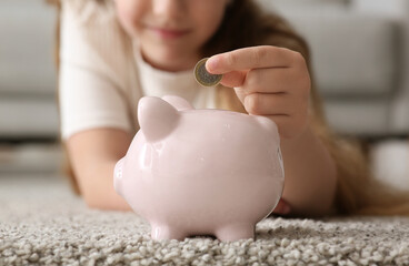 Little girl putting coin into piggy bank at home, closeup. Education savings concept