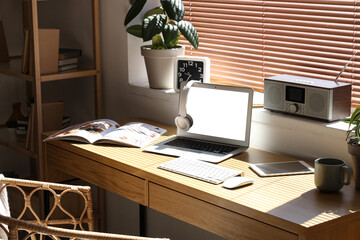 Light office with workplace, modern laptop, houseplants and armchair, closeup