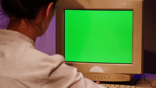 Young woman is typing on old vintage computer keyboard close-up. Work office place concept, old monitor with chroma key screen. Working and chatting in personal old pc computer with green screen.