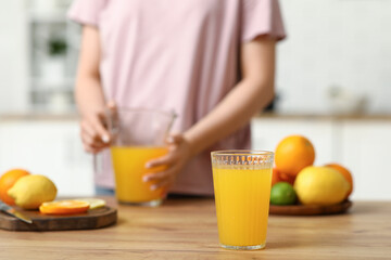 Young woman with jug and glass of fresh orange juice in kitchen