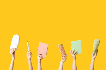 Female hands with pencil cases, notebooks and felt pen on yellow background