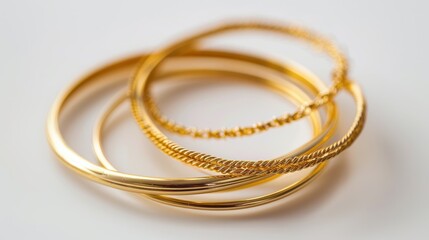Three golden bracelets, featuring different styles and textures, intertwined on a white background