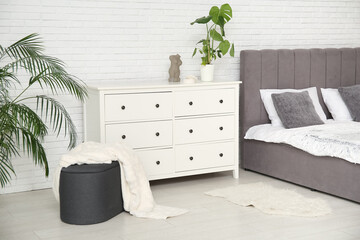 Bed, chest of drawers, houseplants and pouf with plaid in bedroom