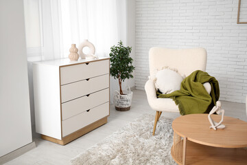 Armchair with cushion, plaid, coffee table and chest of drawers in room