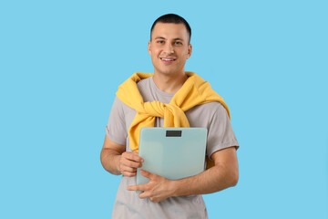 Young man with weight scales on blue background