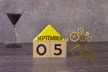 Wooden calendar with the date September 05 and gypsophila flowers on a gray concrete background.