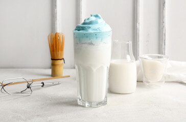 Glass of blue dalgona matcha latte, whisk and bottle of milk on table, closeup