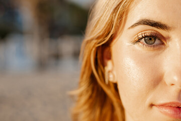 Fototapeta premium Portrait of one happy young beautiful woman smiling looking at the camera with big blue and green eyes. Female girl at the beach close up face.