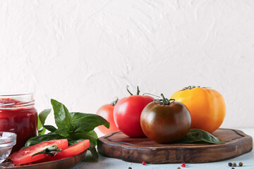 Tomatoes on board with sprig of basil on table against white background. Closeup