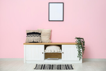 Sideboard with cushions and houseplant near pink wall in room