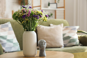 Wild flowers in vase and stone human head on coffee table in living room. Closeup