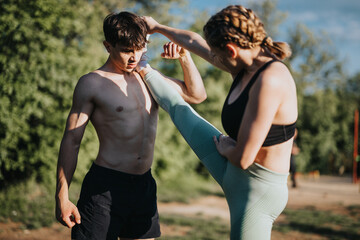 A young woman executes a high kick while training outdoors with a male partner. Demonstrates focus,...