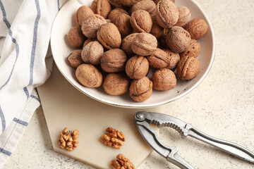 Bowl with tasty walnuts and nutcracker on white background